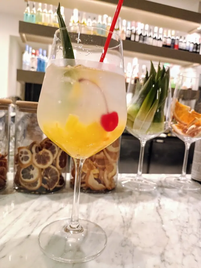 A spritz with a cherry and pineapple leaf on the marble bar
