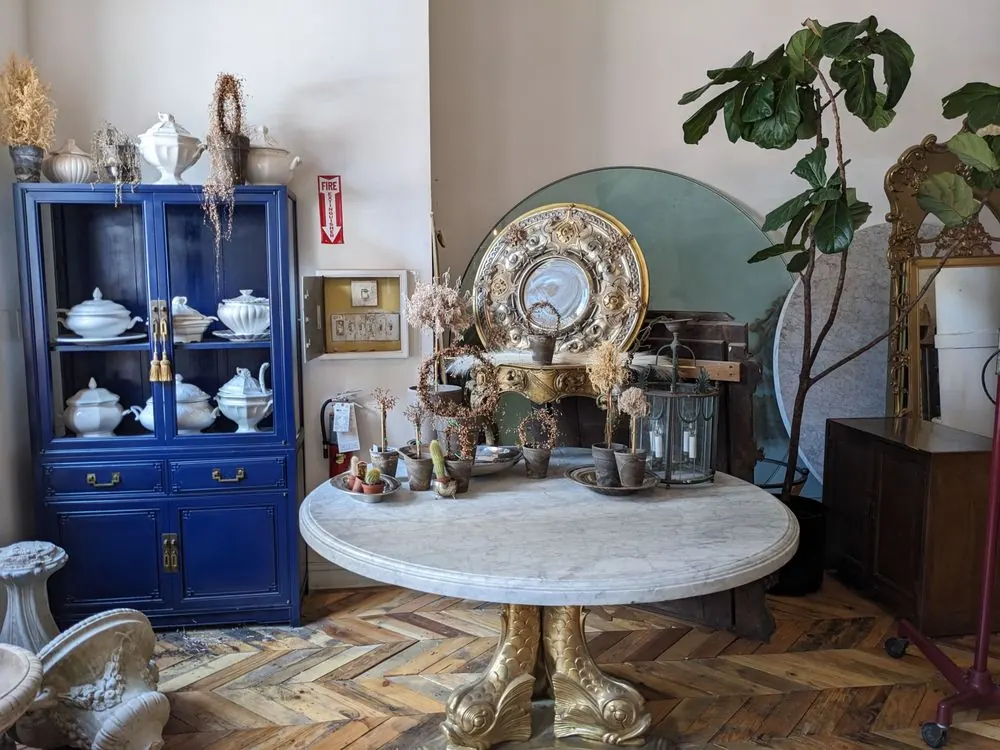 A blue china cabinet beside a round marble table set with silver and brass