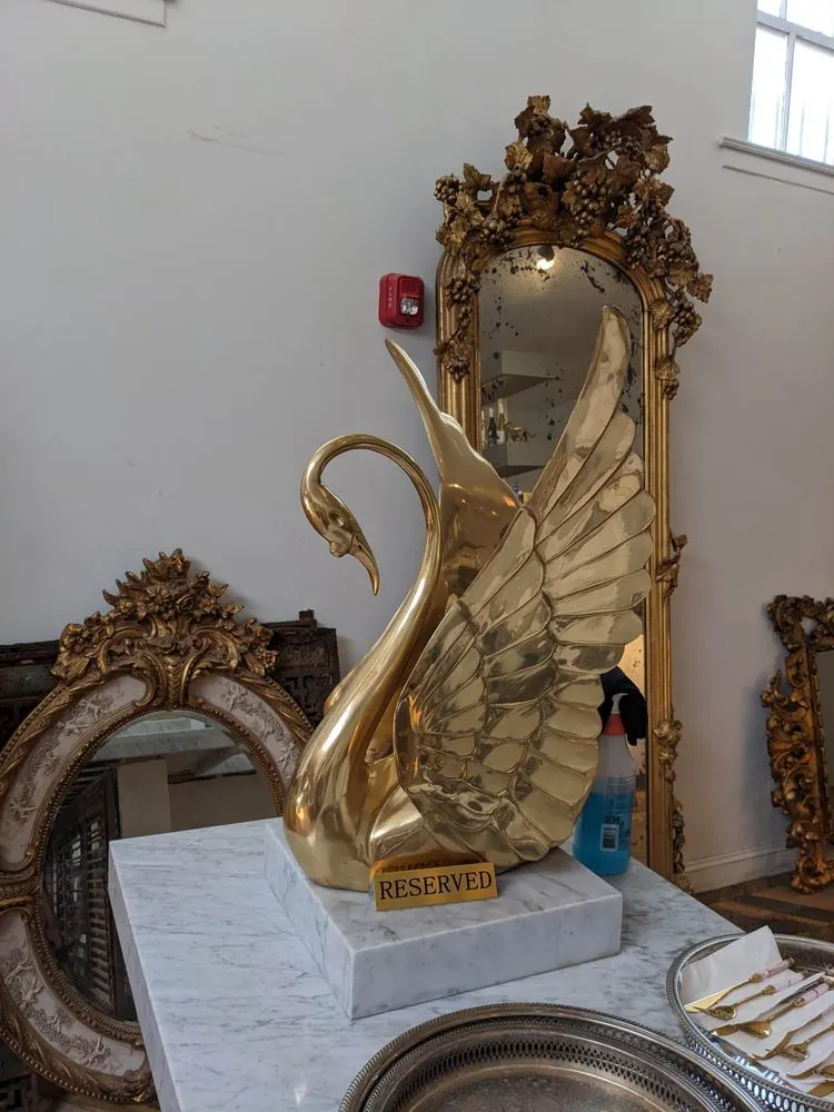 A gold swan sculpture on a marble table before a gilt mirror