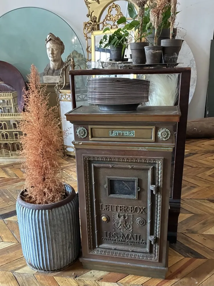 An antique brass letter box beside a marble bust and a dried pampas plant