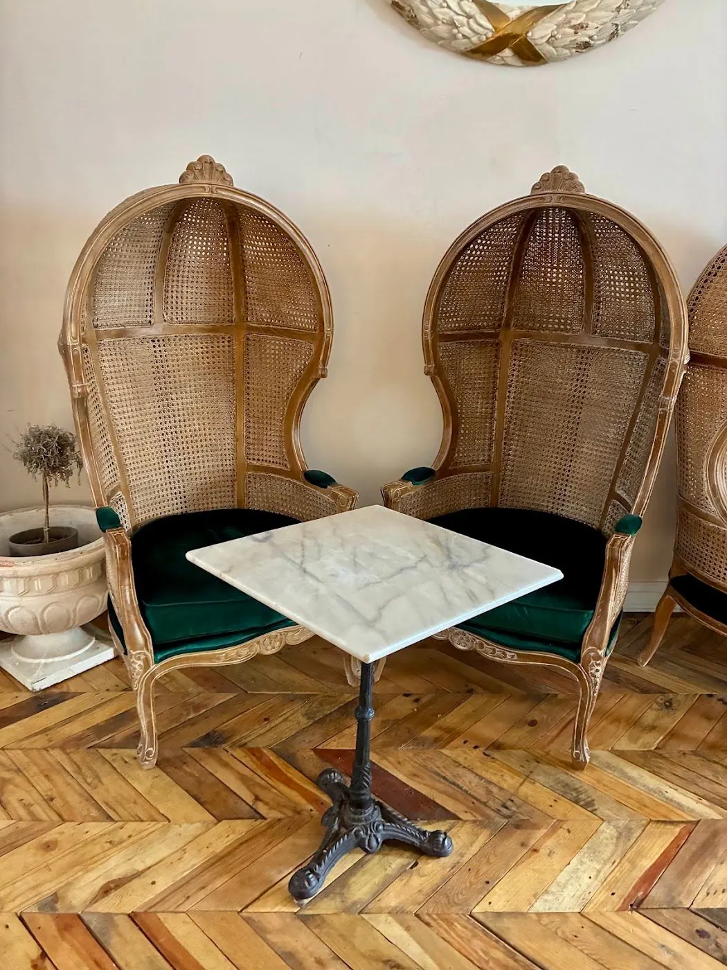 Two hooded cane porter chairs with green velvet seats at a marble table