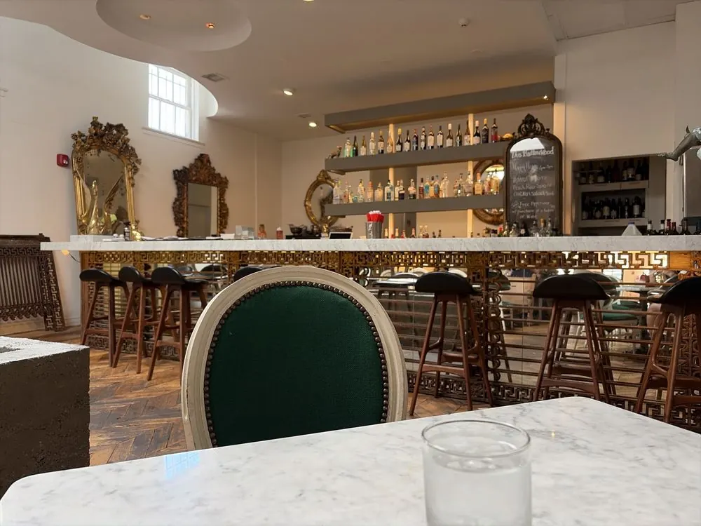 The marble bar with wooden stools, bottle shelves and gilt mirrors on the white walls