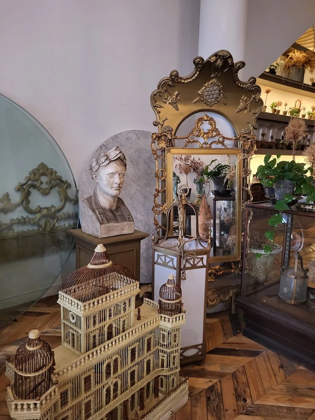 A plaster bust and a gilt mirror behind a birdcage shaped like a building