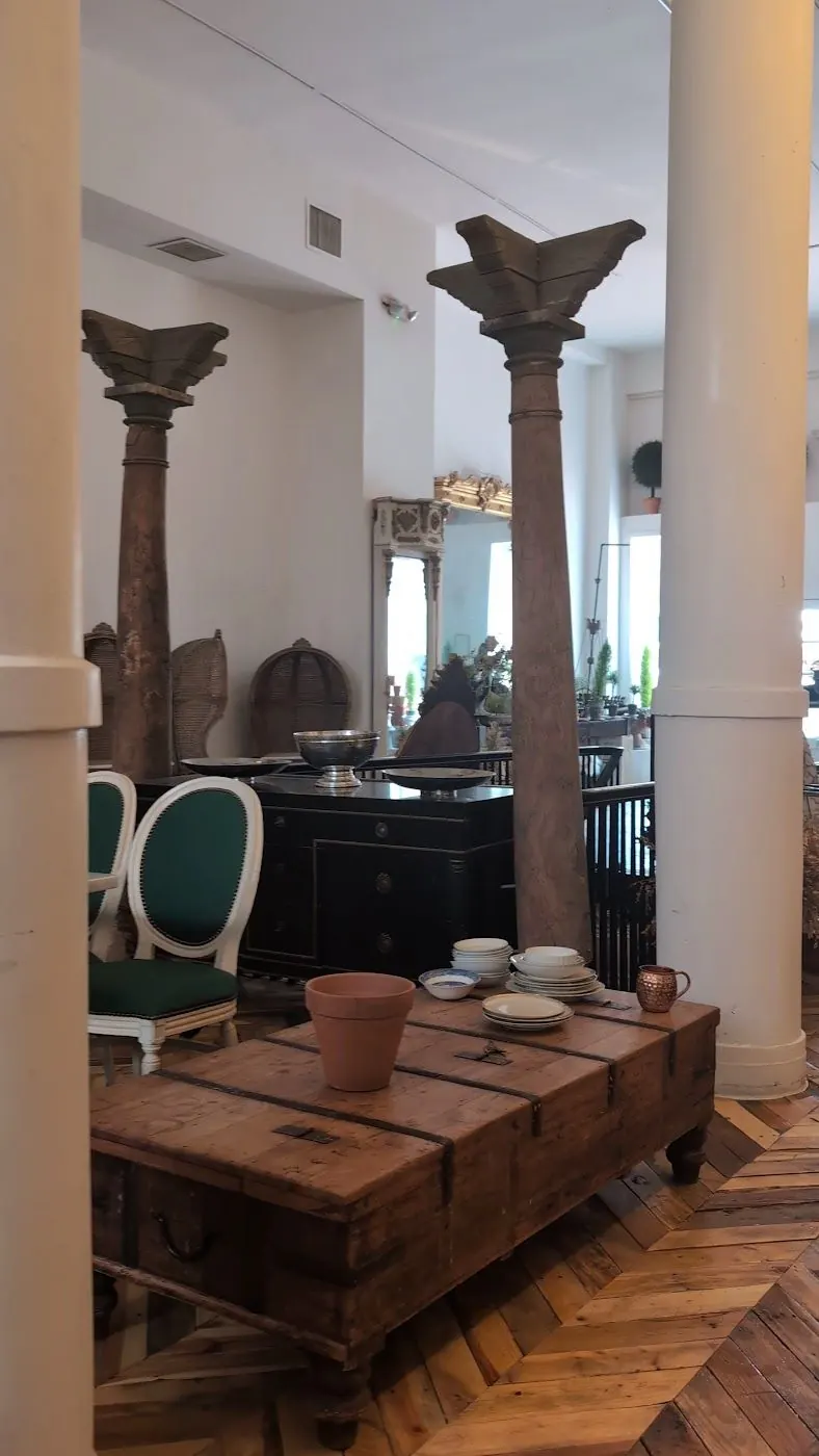 Two antique carved wooden columns beside a white column and a low wooden trunk used as a table