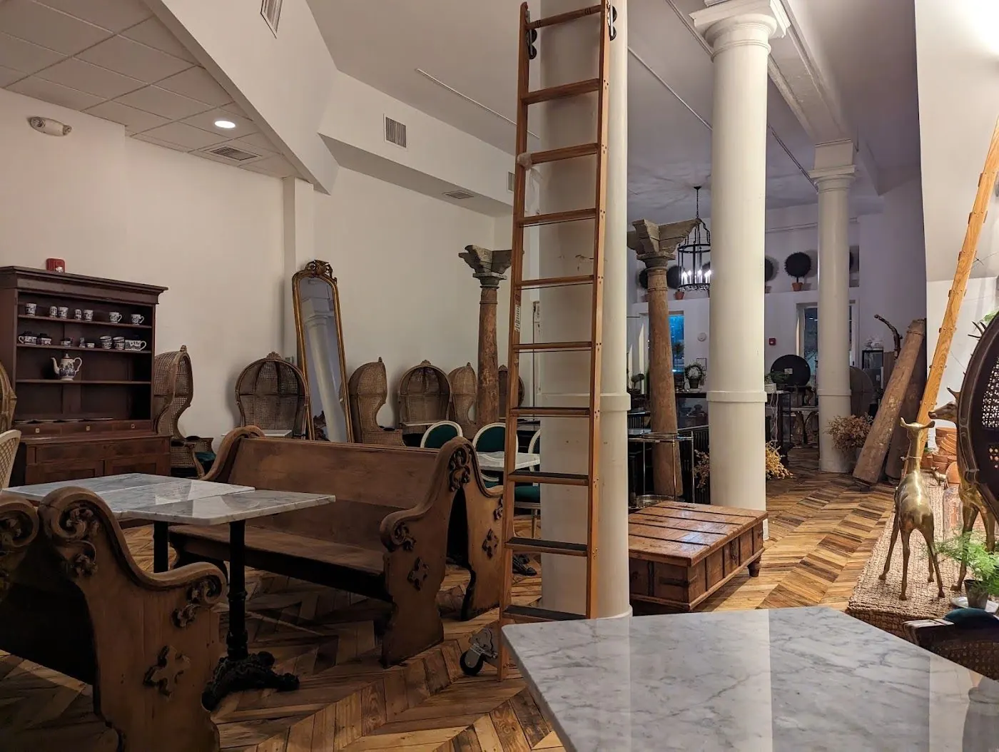 Carved wooden church pews at marble tables beside a library ladder and white columns