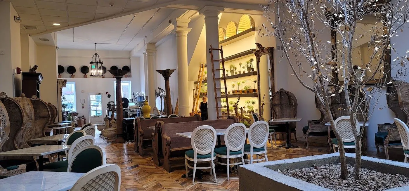 Wide view of the dining room with church pews, porter chairs, white columns and lit shelves with a library ladder