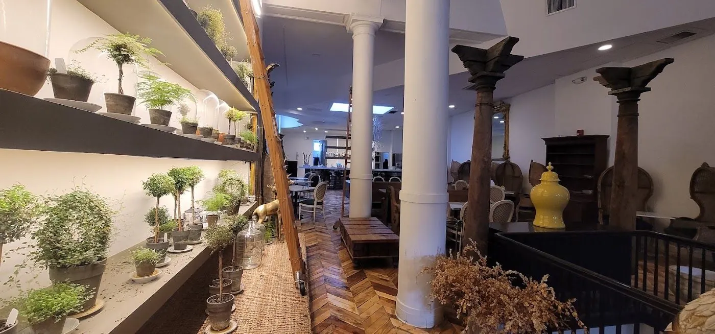Shelves of potted topiaries running toward white columns and carved wooden columns