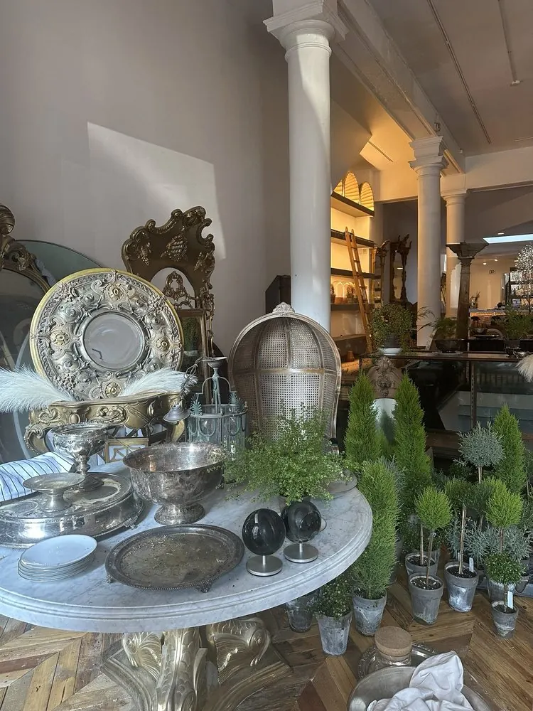 A marble table set with antique silver platters and bowls among small potted evergreens